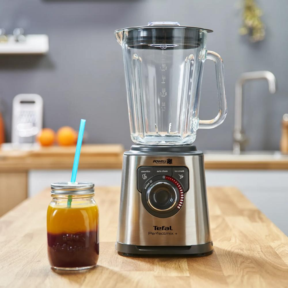 Srebrny blender stoi obok szklanki soku z niebieską słomką.