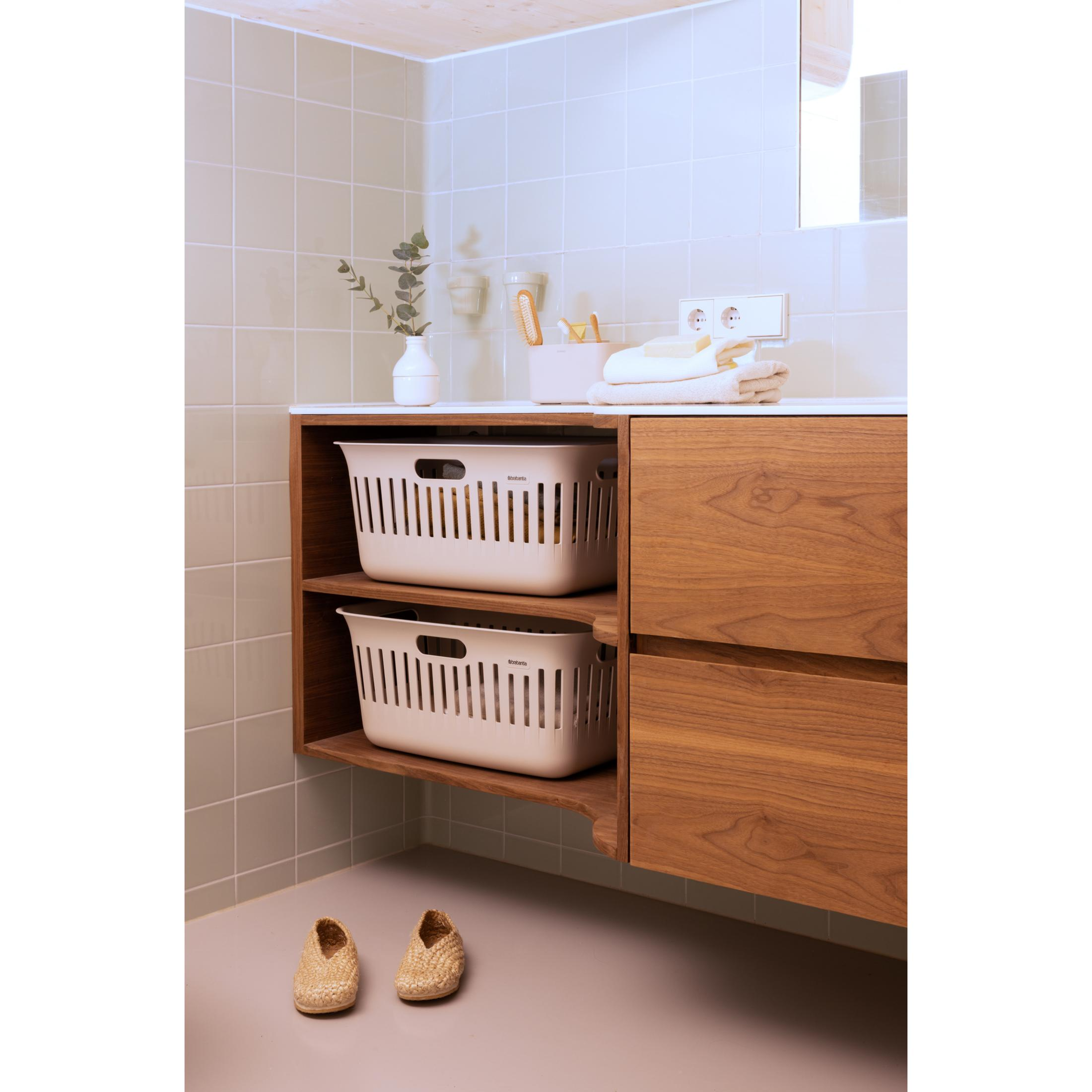 Two beige laundry baskets on a shelf above two straw shoes on the floor.
