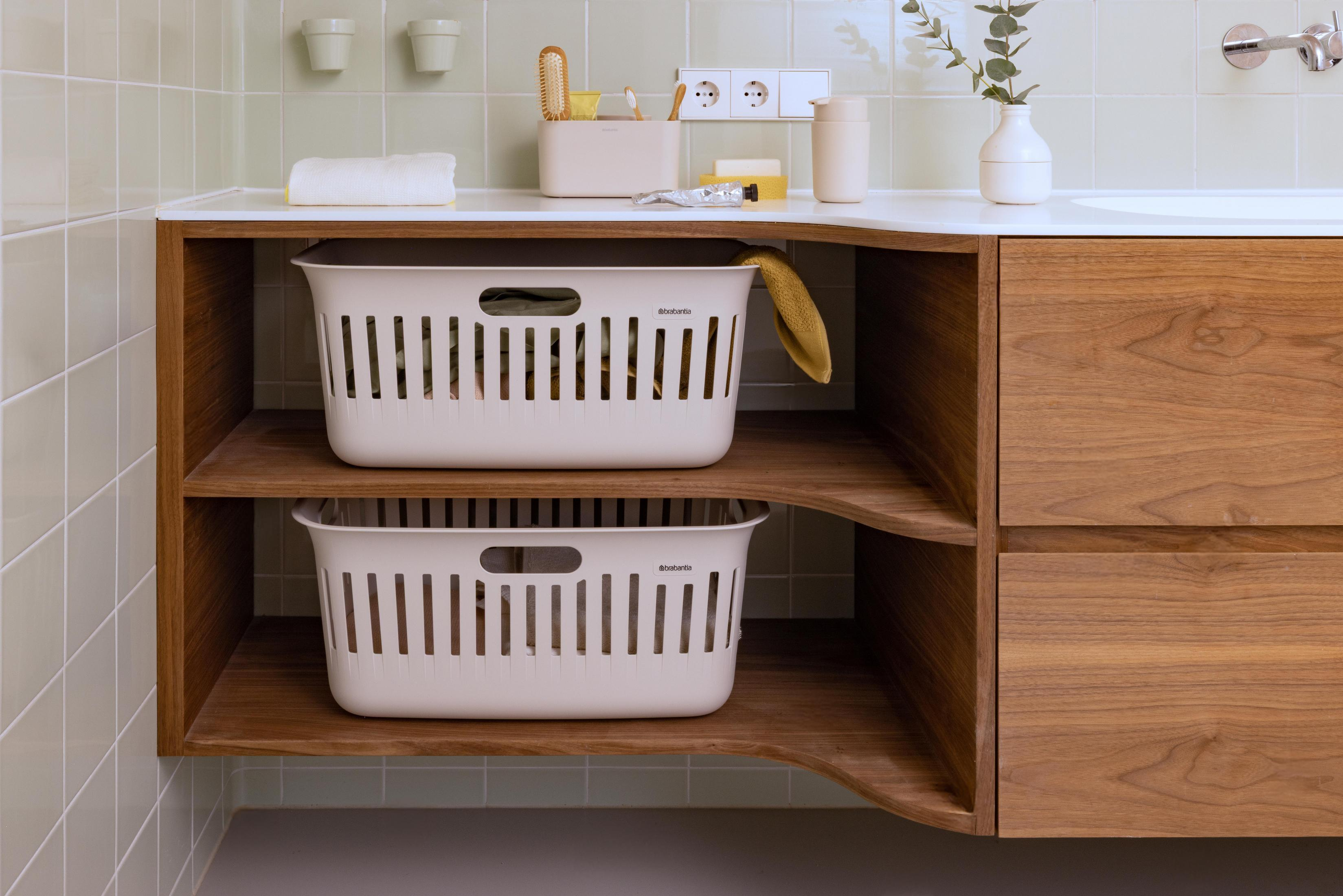Two white laundry baskets on a wooden shelf next to a wooden cabinet.