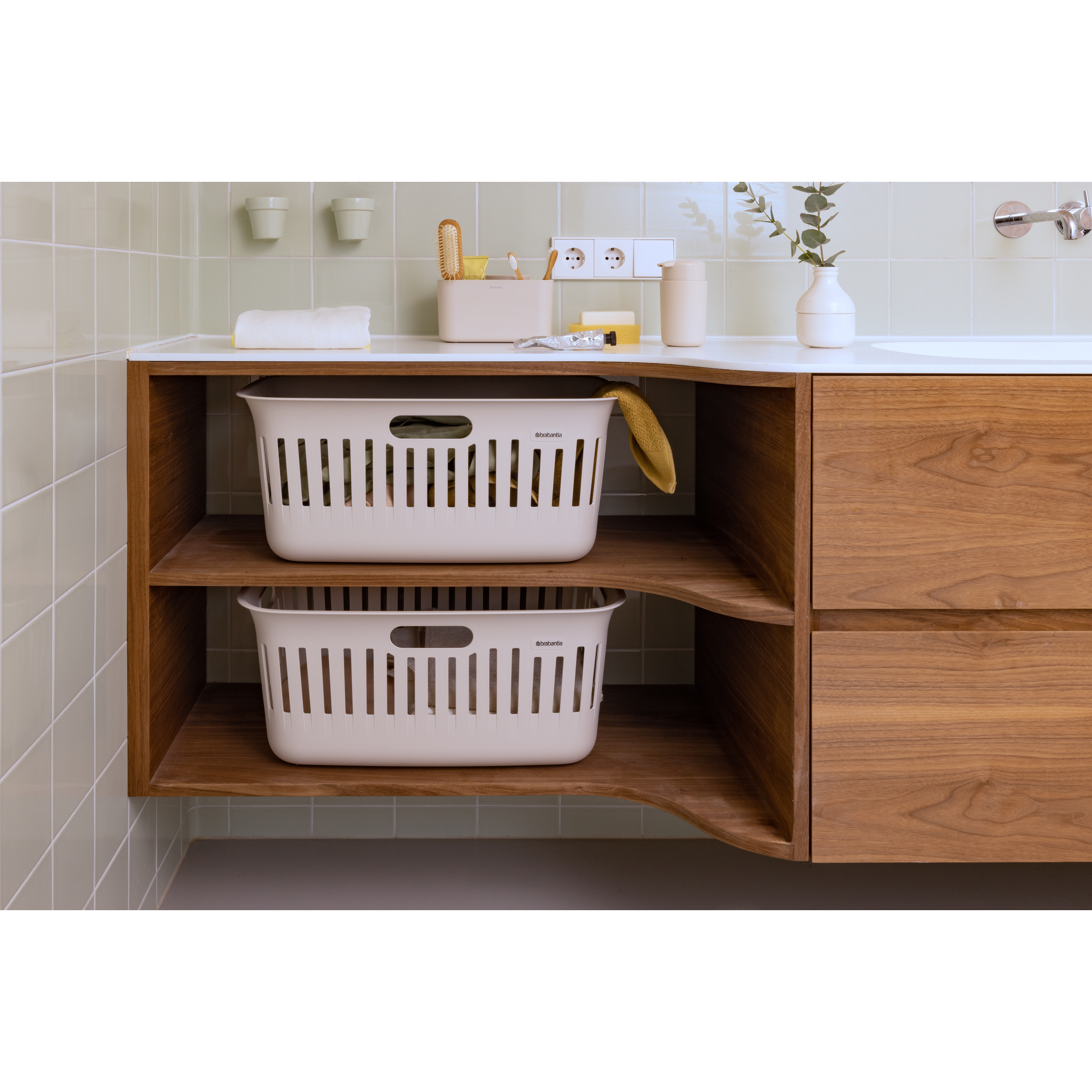 Two white plastic laundry baskets sit on a wooden shelf under a sink.