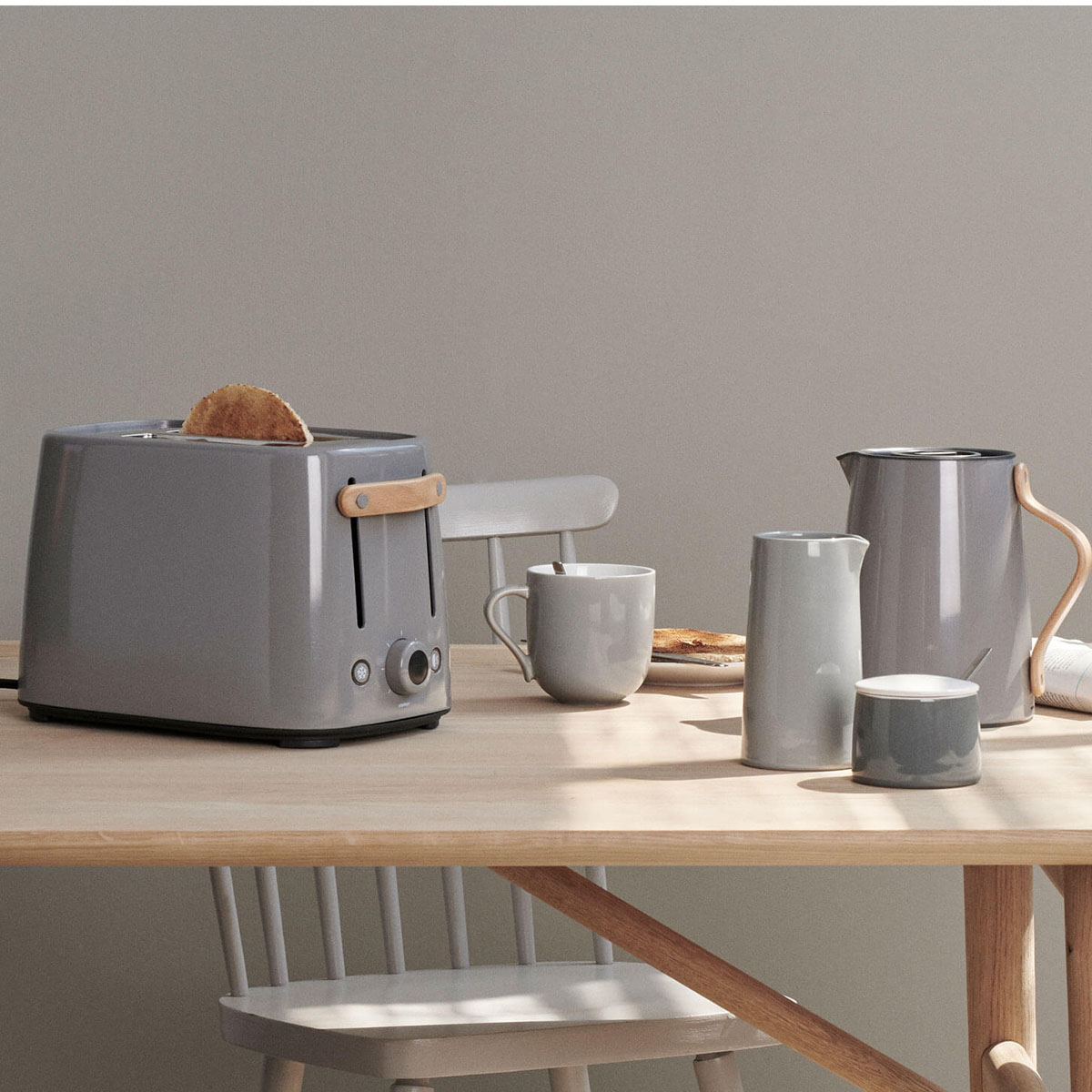 Tostapane grigio con toast, tazza, caraffa e zuccheriera su tavolo legno.