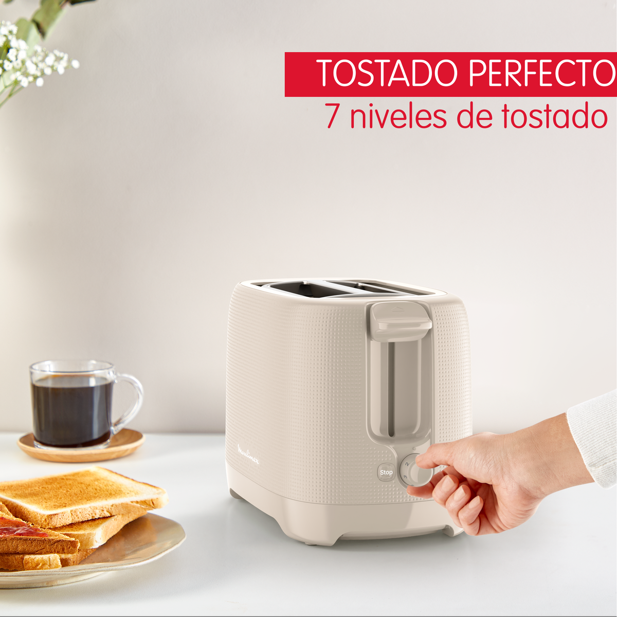Un tostapane beige con una mano che gira la manopola. Toast e caffè nelle vicinanze.