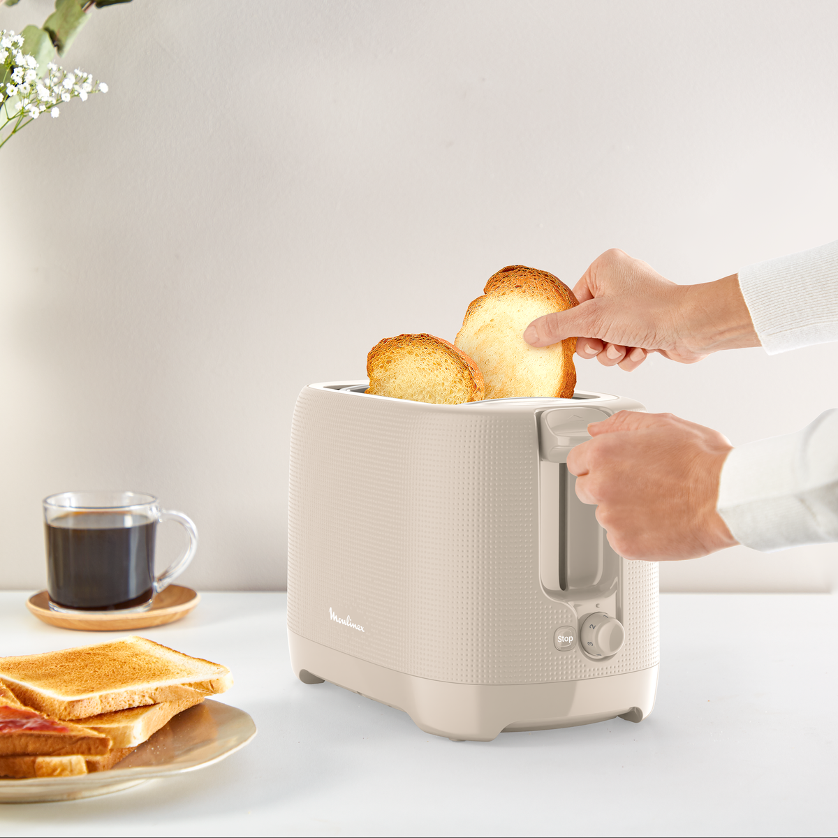 Un tostapane beige con toast che viene inserito. Caffè e toast nelle vicinanze.
