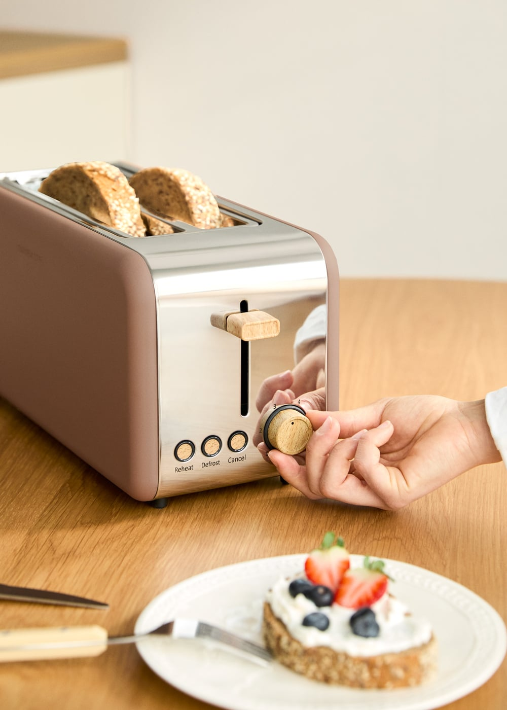 Una tostadora marrón con dos rebanadas de pan, una mano girando la perilla.