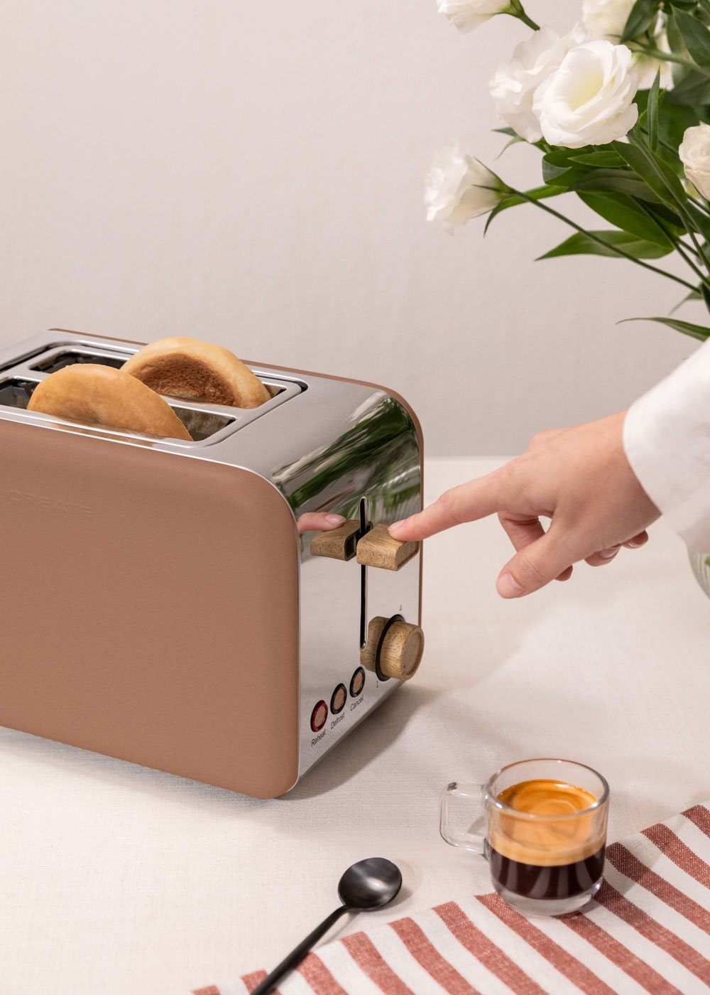 Tostadora marrón con dos bollos, mano presionando palanca, café cerca.