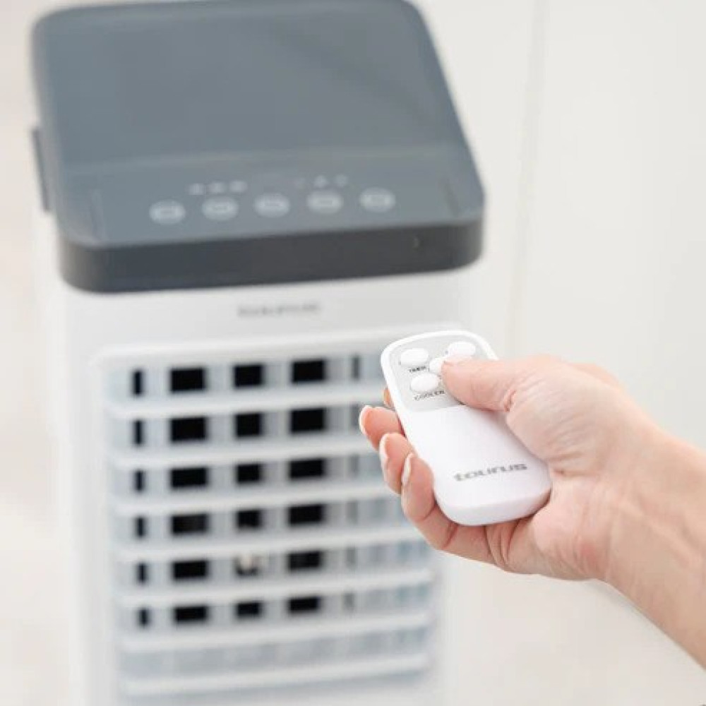 Una mano tiene un telecomando bianco davanti a un condizionatore d'aria bianco.