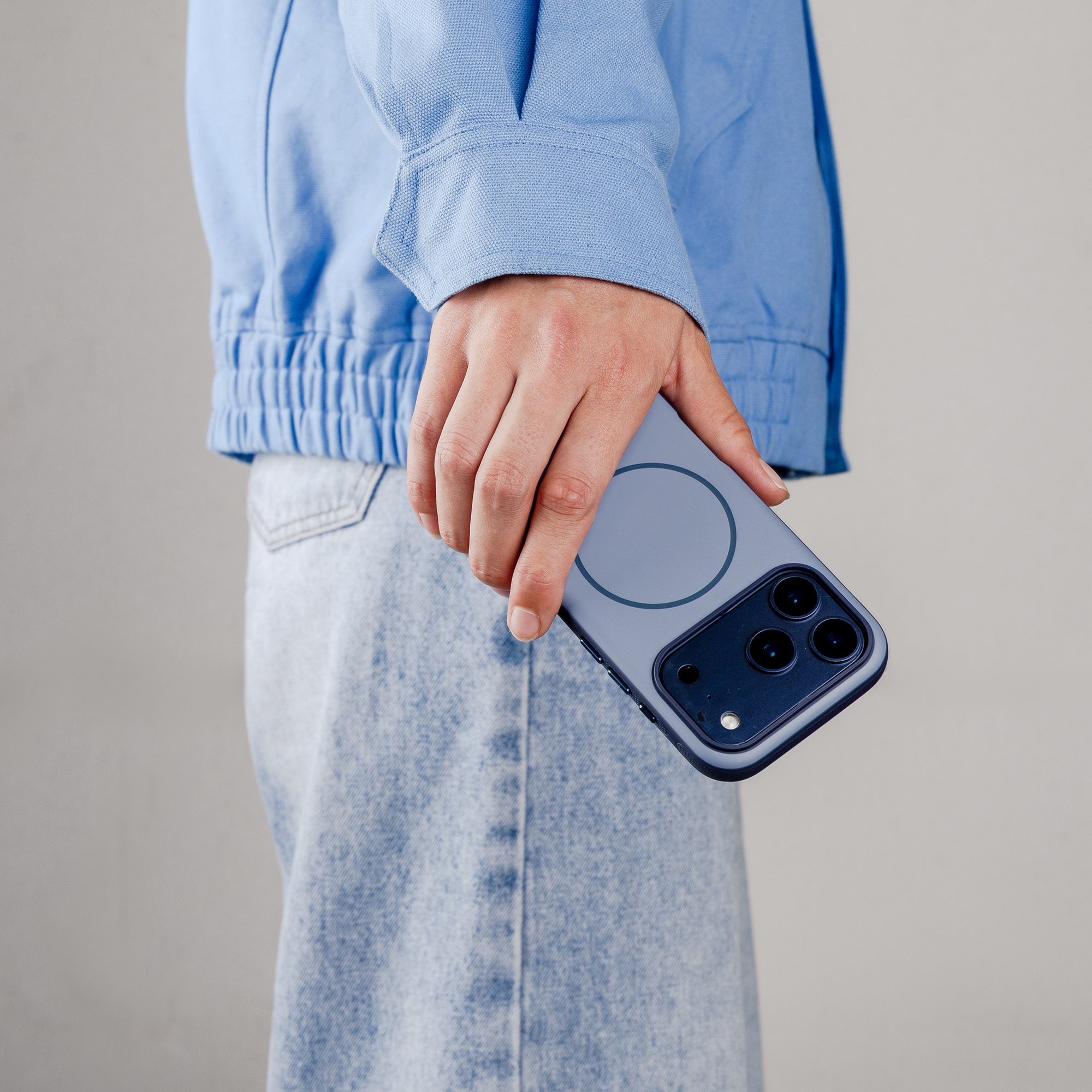 Een hand houdt een blauwe smartphone vast met drie camera's en een cirkel op de achterkant.
