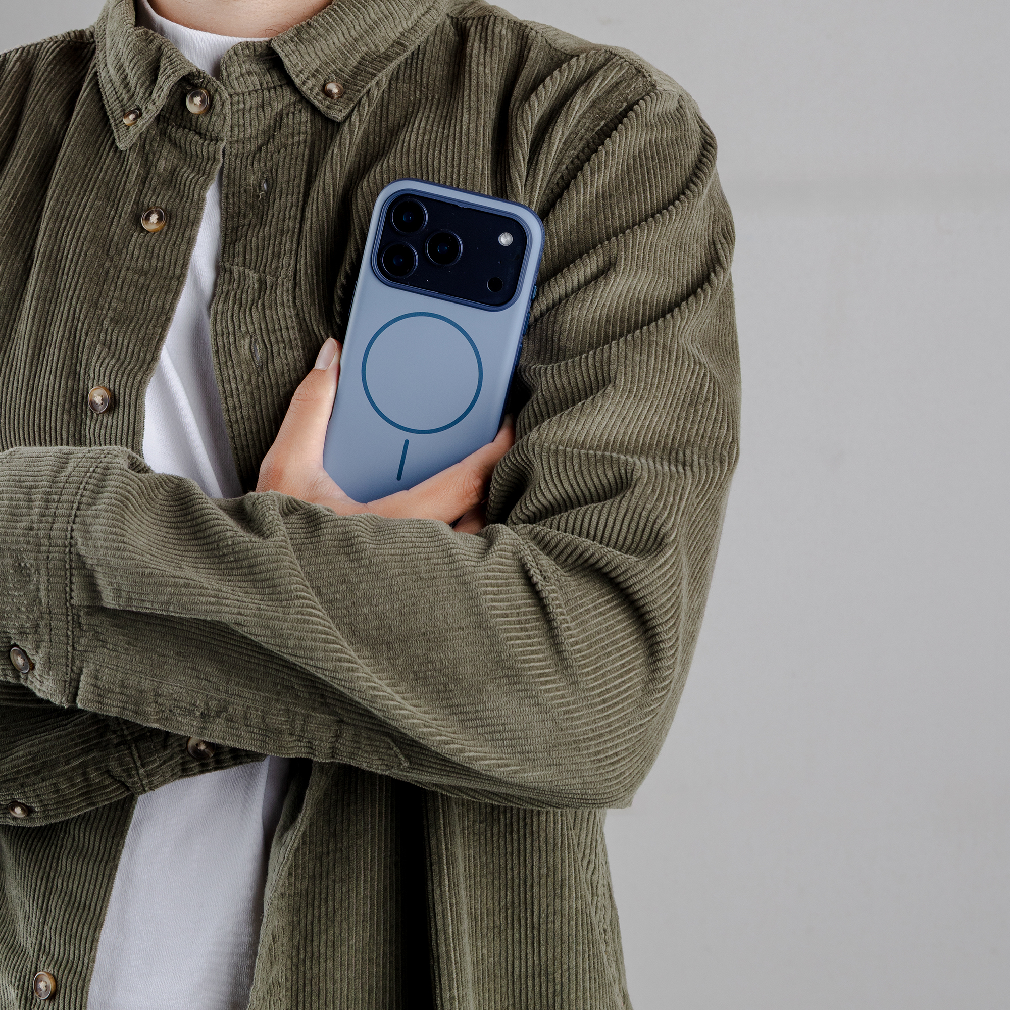 Persoon in corduroy jas houdt een blauwe telefoon met drie camera's vast.