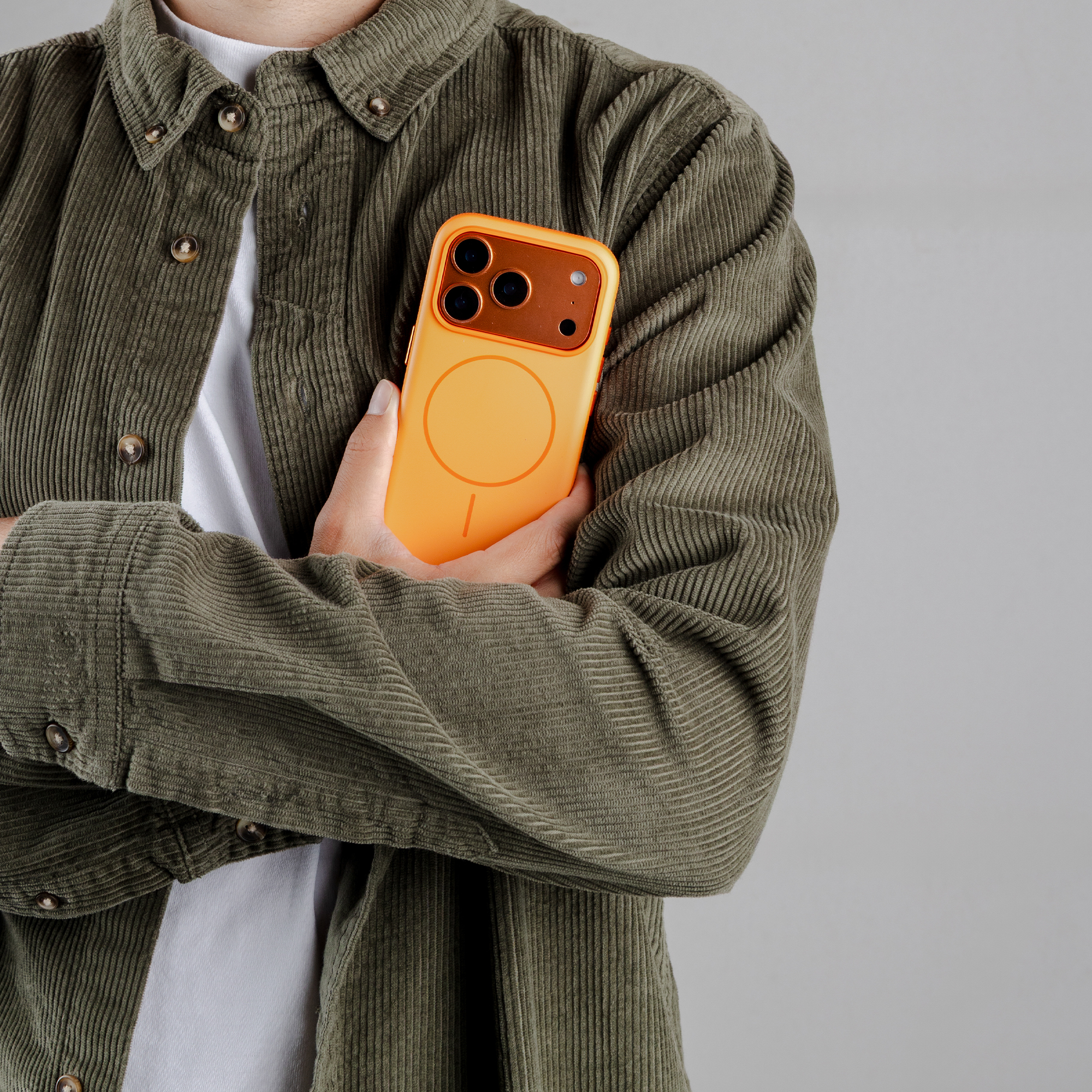 Een persoon draagt een olijfgroen corduroy shirt over een wit T-shirt, met een oranje telefoon in de hand.