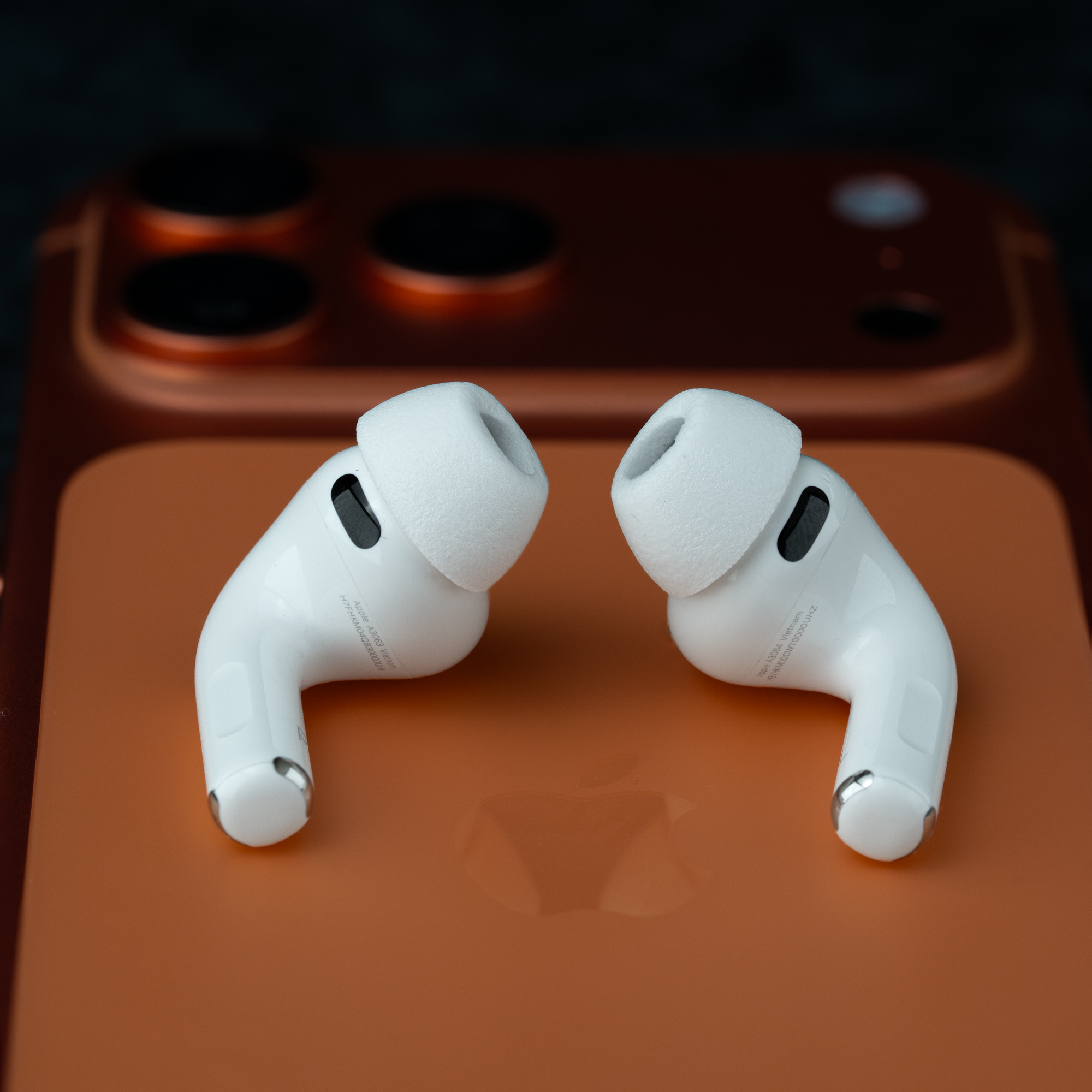 Zwei weiße AirPods liegen auf einem orangefarbenen iPhone mit Apple-Logo.