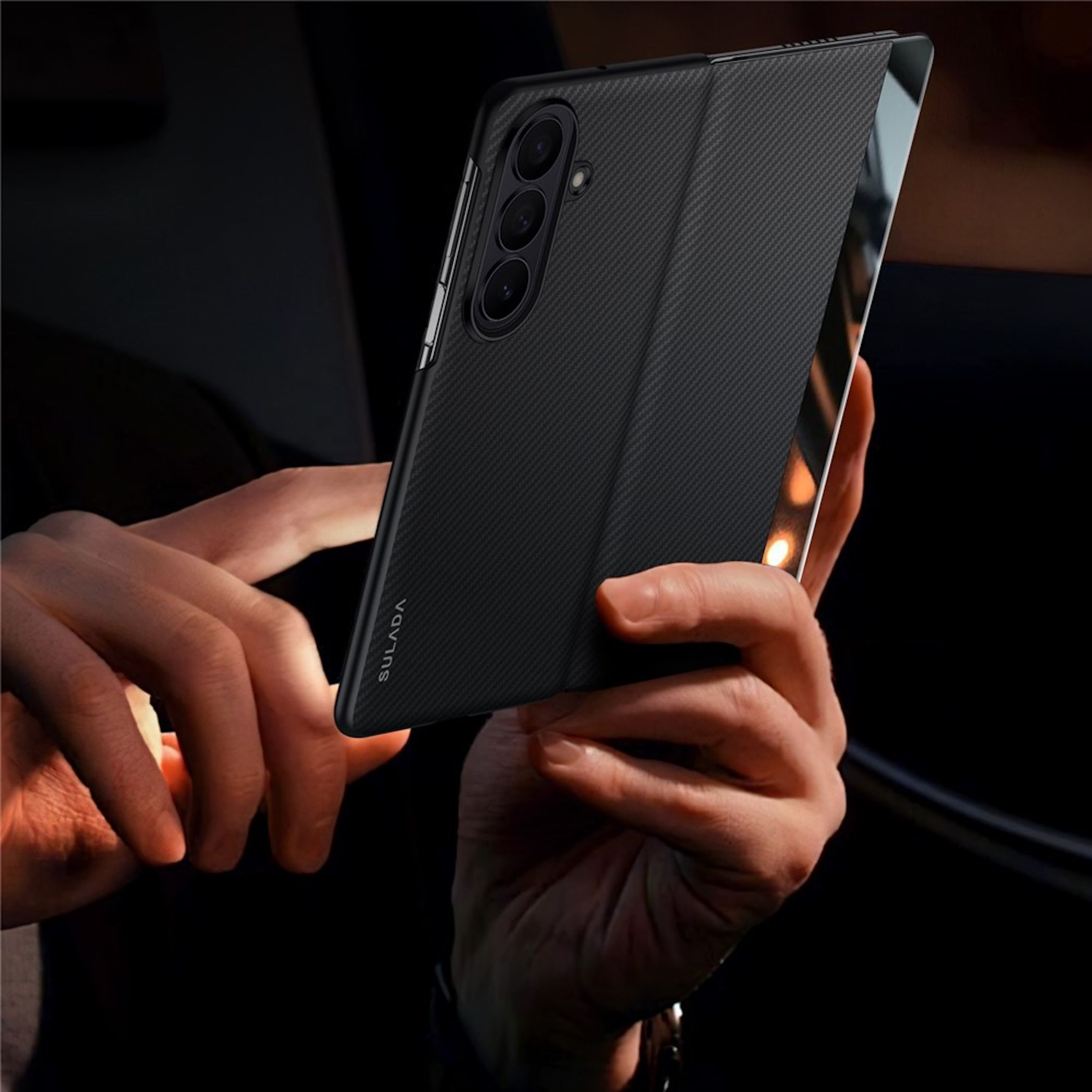 Schwarzes Handy mit Carbon-Muster in Händen, Kamera auf der Rückseite.