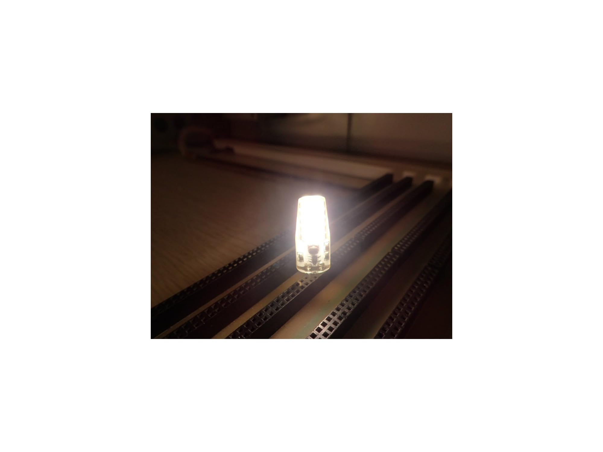 Eine leuchtende LED-Lampe auf einer Holzoberfläche, umgeben von dunklen Schienen.