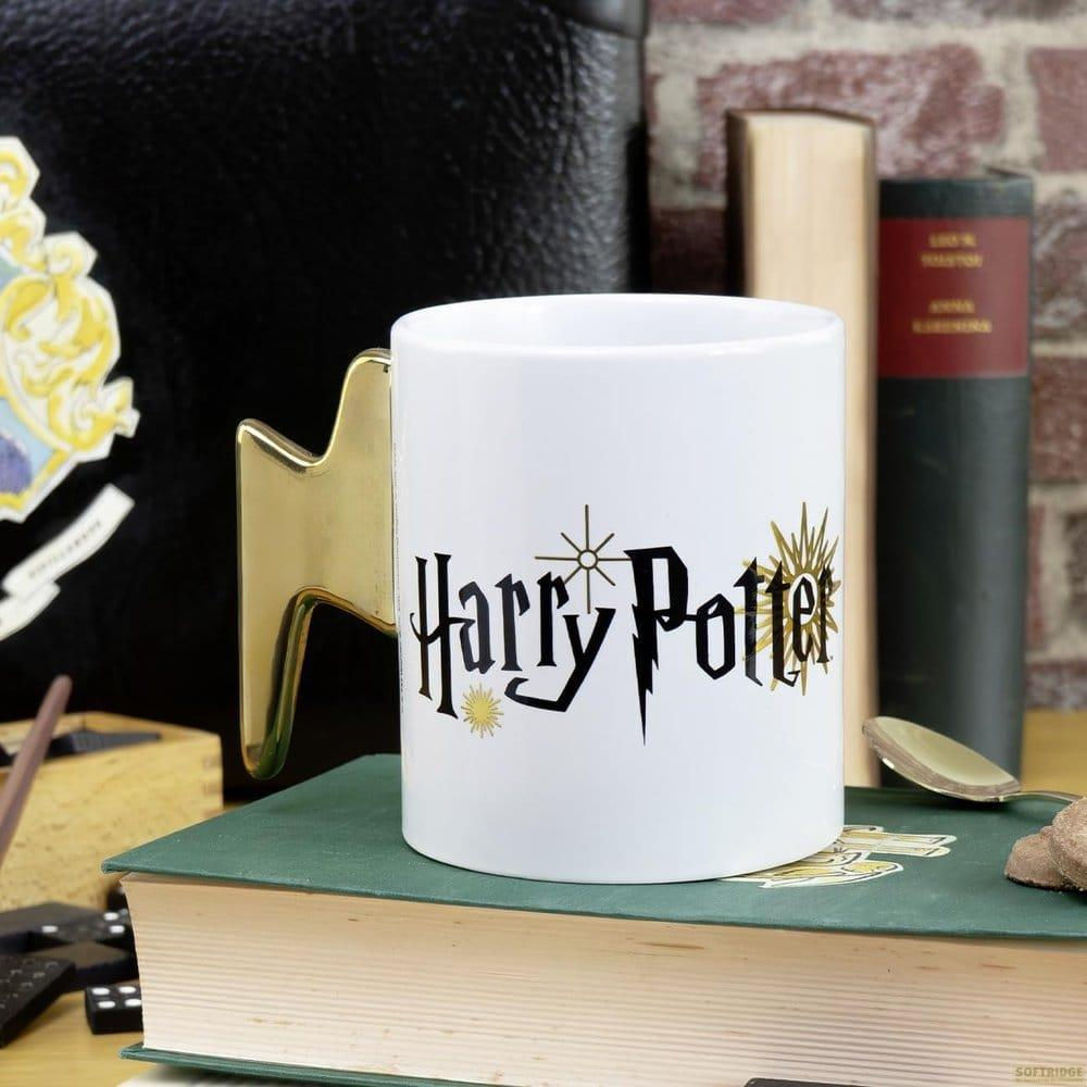 Weiße Tasse mit Harry Potter Schriftzug und goldenem Griff, auf Büchern platziert.