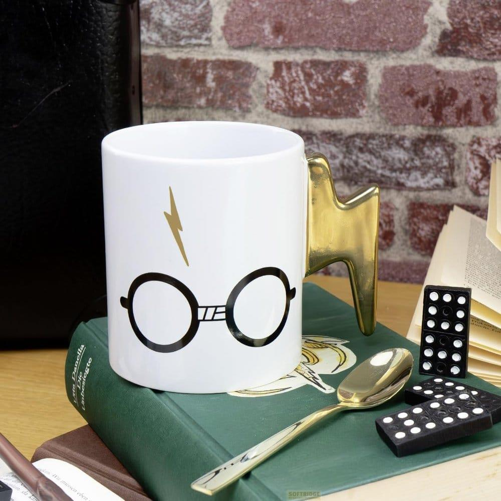 Weiße Tasse mit Brillen- und Blitzmuster, goldener Griff, Löffel, Dominosteine, Bücher.
