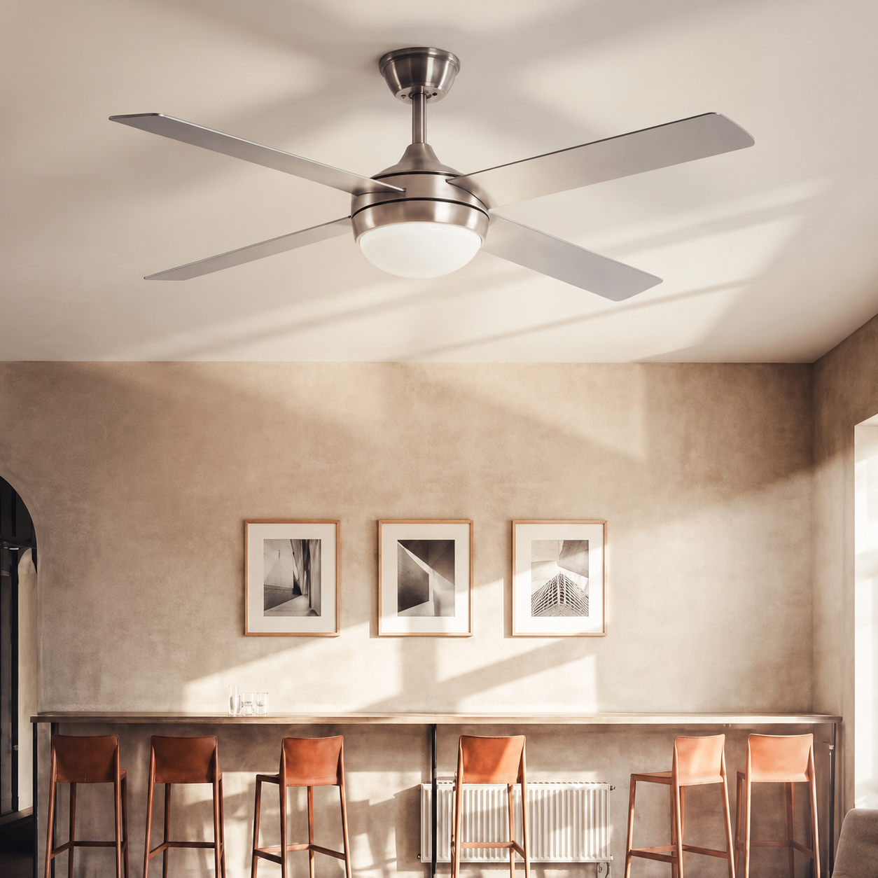 Un ventilador de techo con luz sobre un mostrador largo con cuatro taburetes y arte en la pared.