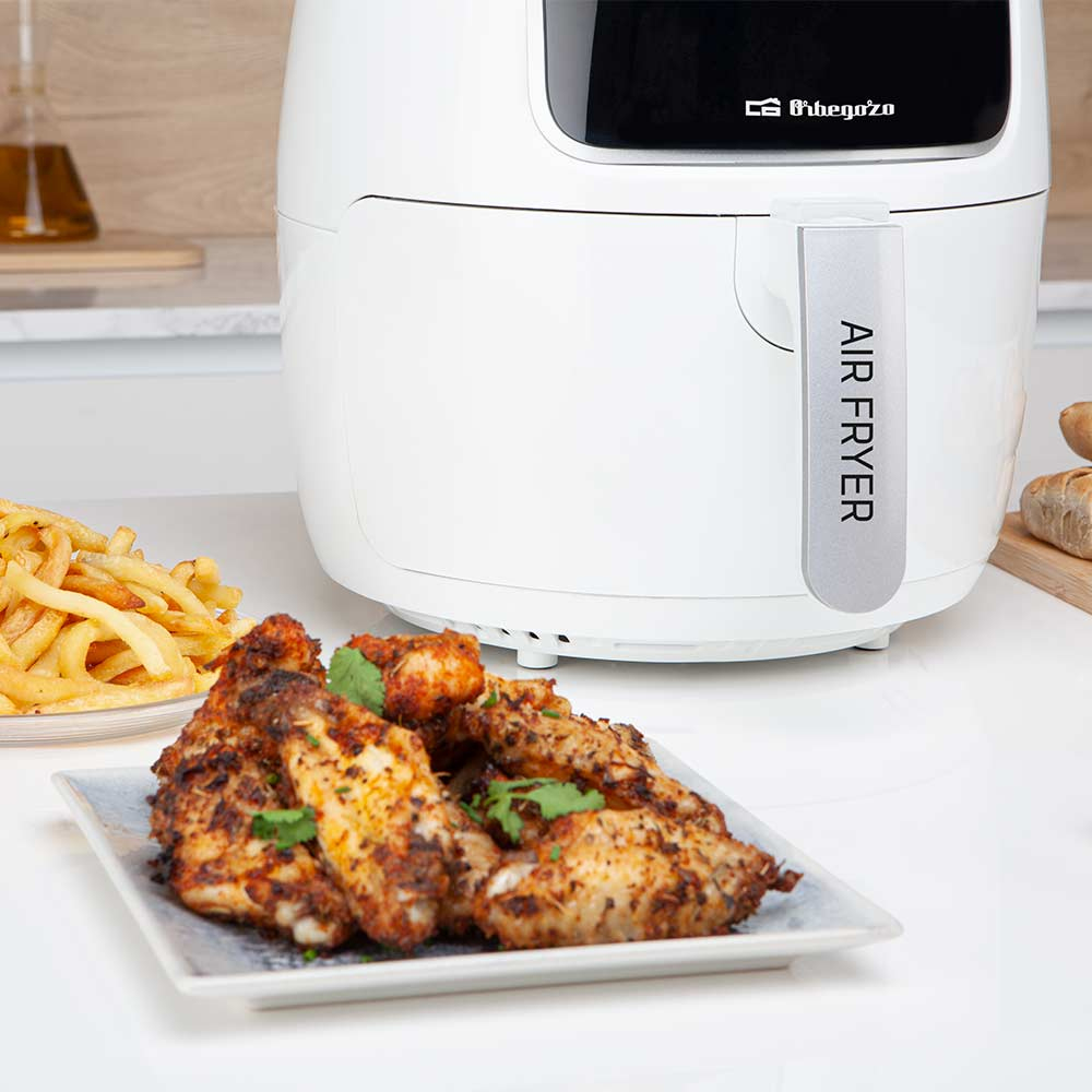 Una friggitrice ad aria bianca accanto a un piatto di alette di pollo e patatine.