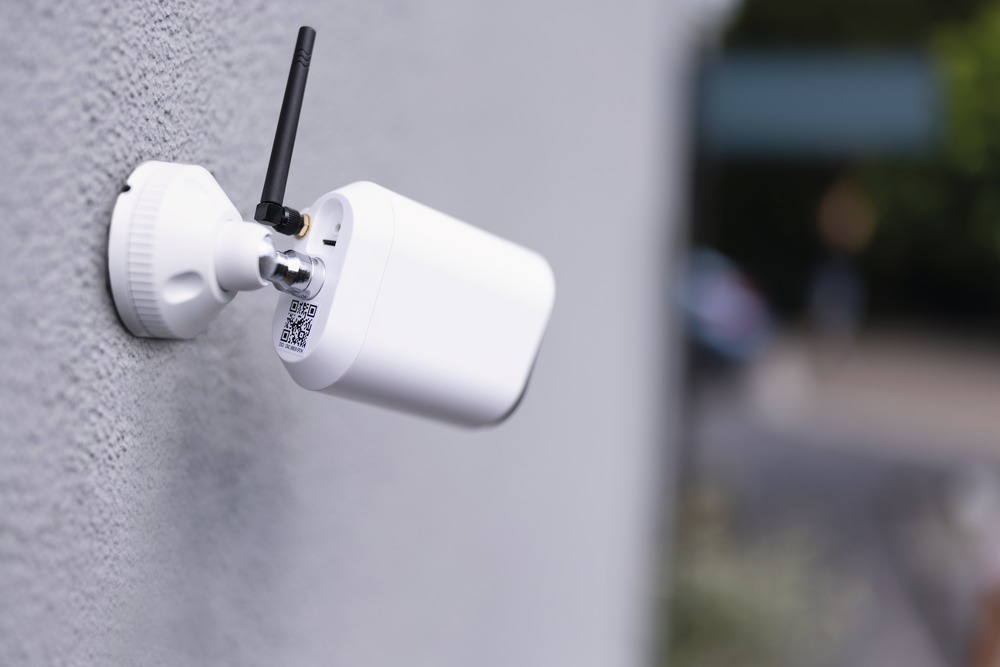 Une caméra de sécurité blanche avec une antenne est fixée à un mur gris.