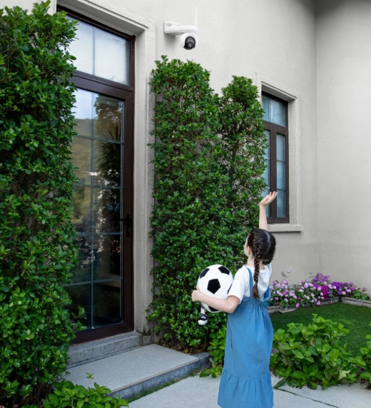 Ein Mädchen mit einem Fußball vor einem Haus, eine Kamera ist oben angebracht.
