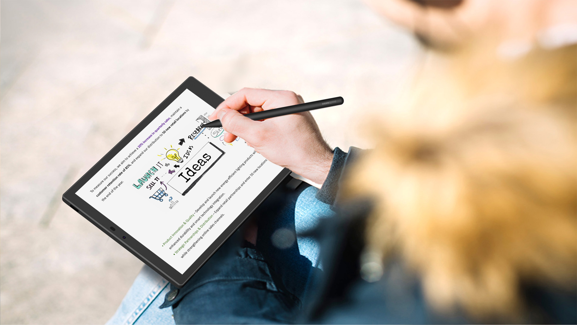 Uomo scrive su tablet con stilo. Visibile un business plan con idee, vendite e ricerca.