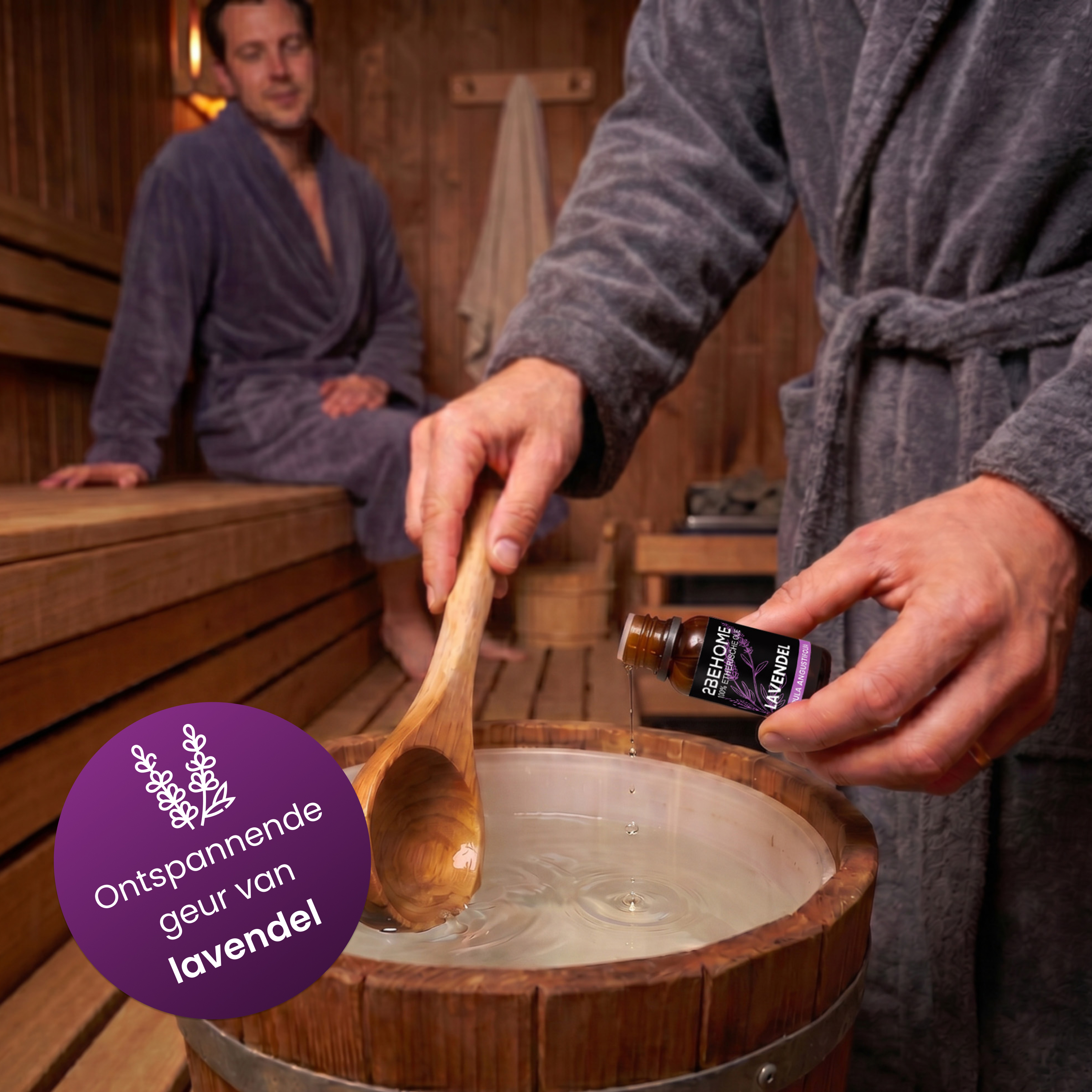 Mann gibt Lavendelöl in ein Holzeimer mit Wasser, neben einem Mann in einem Bademantel.