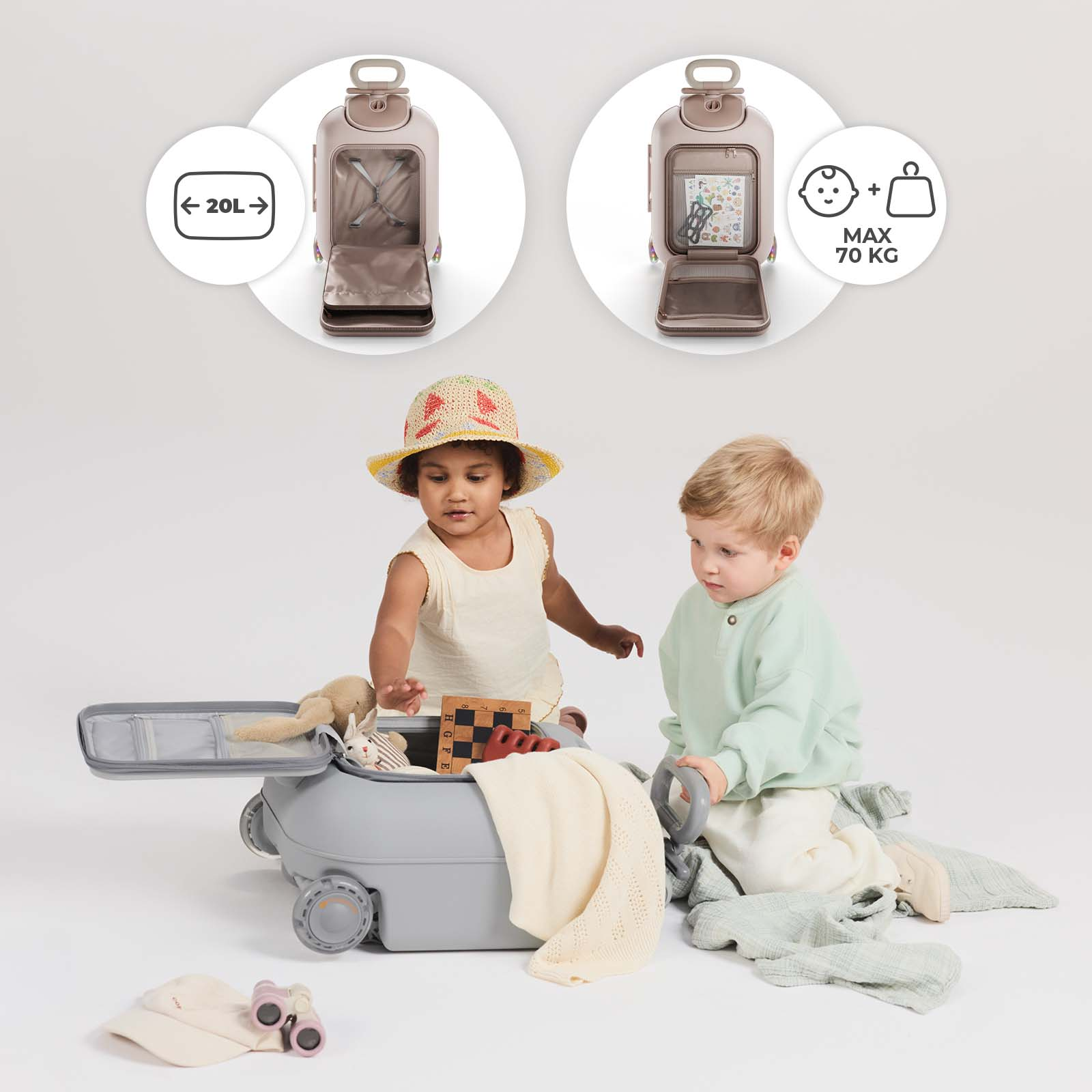 Zwei Kleinkinder spielen mit einem grauen Rollkoffer voller Spielzeug und Decken.