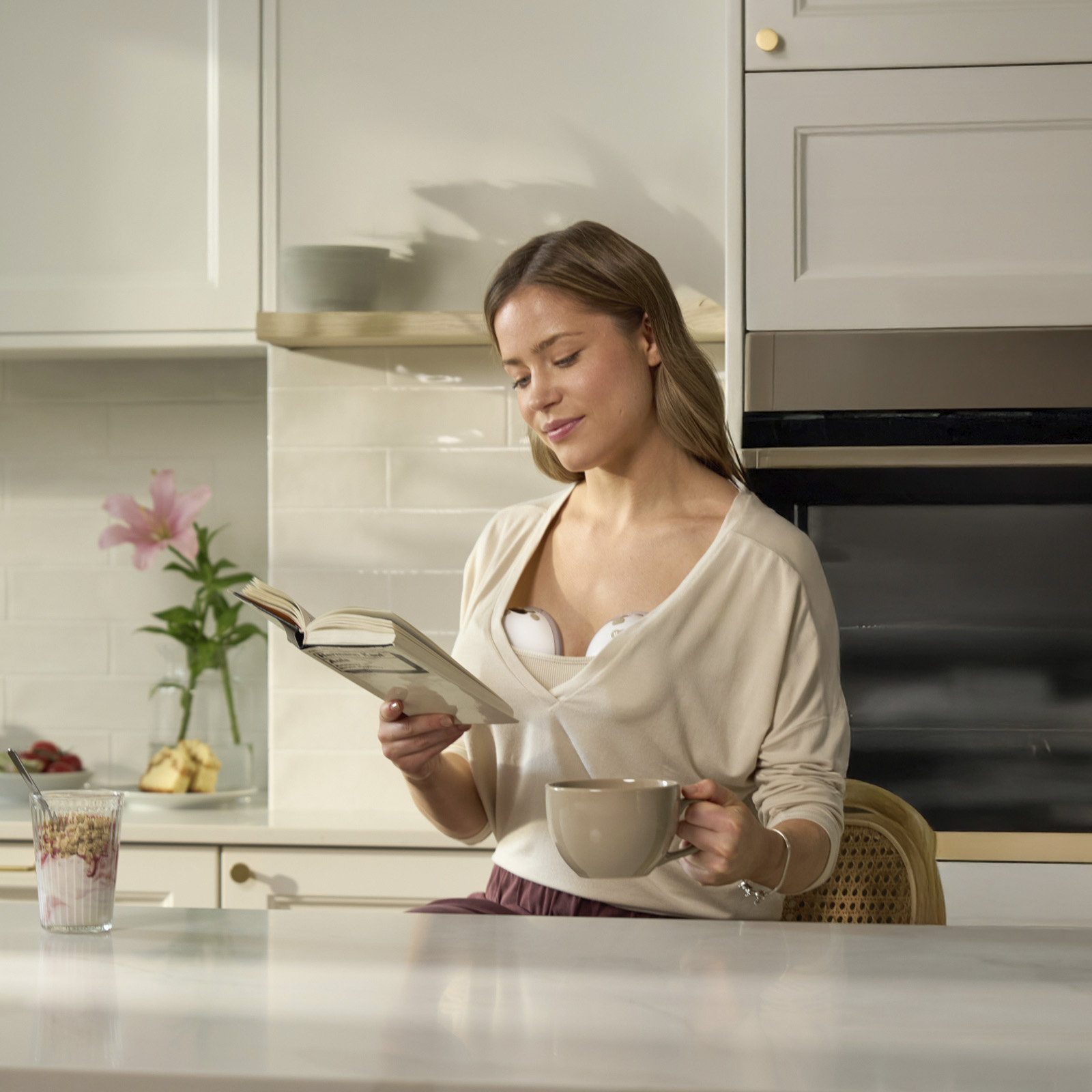 Eine Frau liest ein Buch und trinkt Kaffee in einer Küche mit Frühstück auf der Ablage.