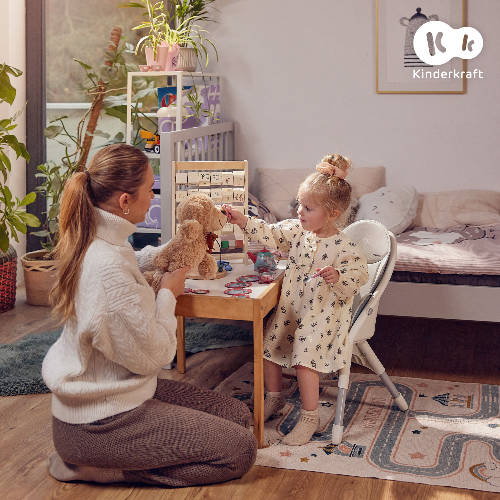 Eine Frau und ein kleines Mädchen spielen mit einem Teddybär an einem Holztisch.