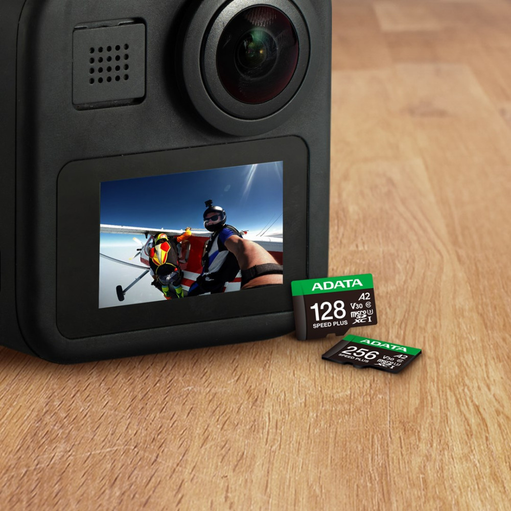 Kamera akcji z ekranem pokazującym skoczków spadochronowych, obok kart microSD ADATA na drewnie.