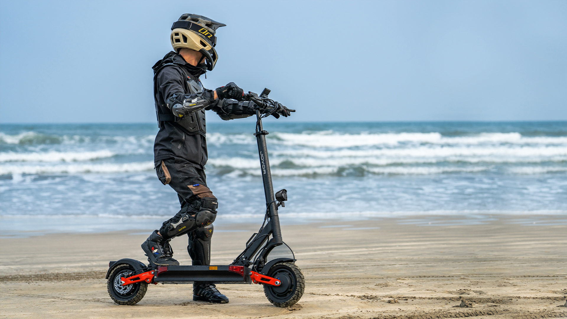 Uomo in abbigliamento protettivo su scooter elettrico in spiaggia.