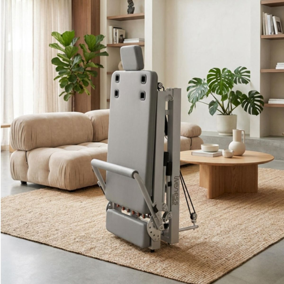 A gray Pilates reformer machine stands on a rug in front of a sofa and coffee table.