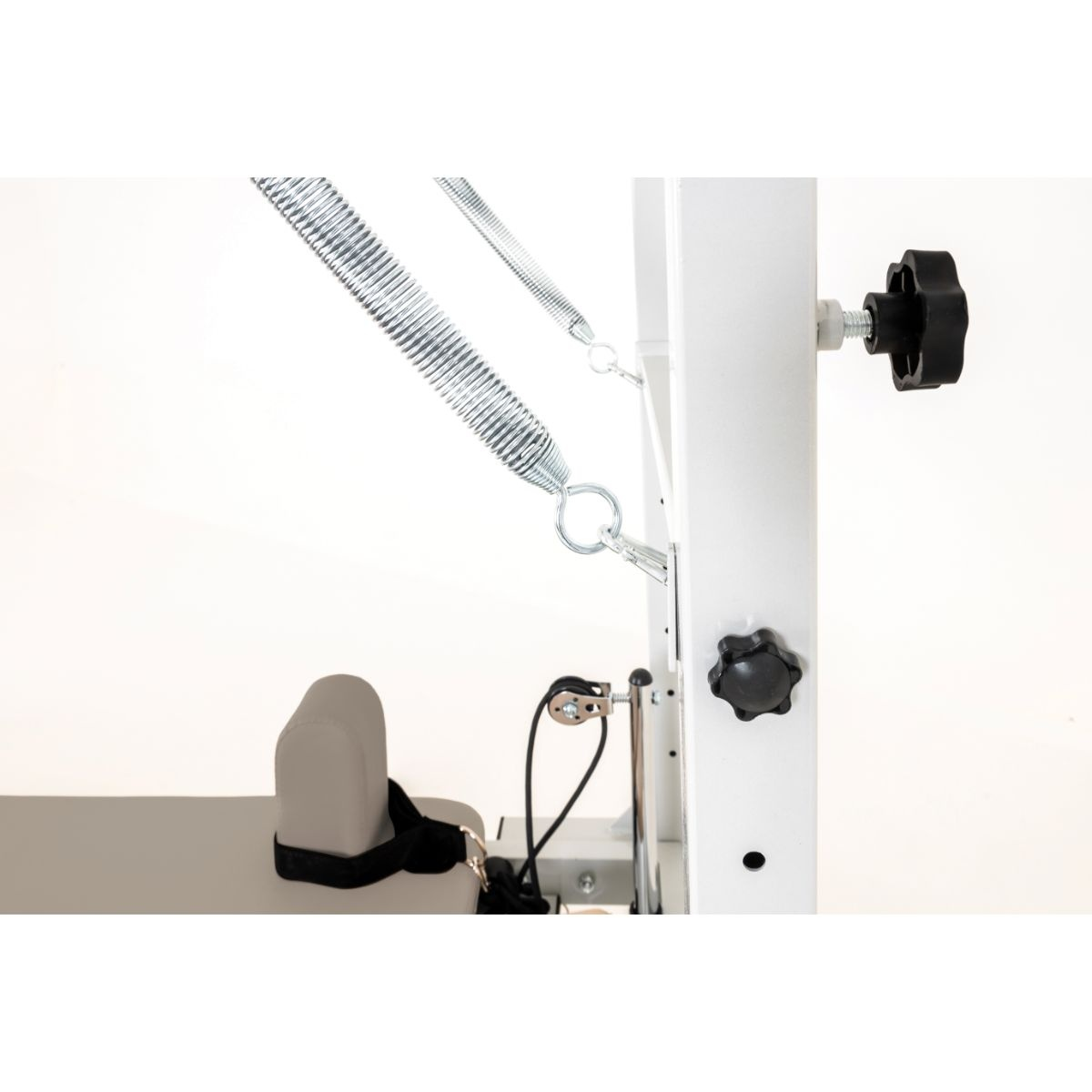 Close-up van witte Pilates-apparatuur met veren, zitting en zwarte knoppen.