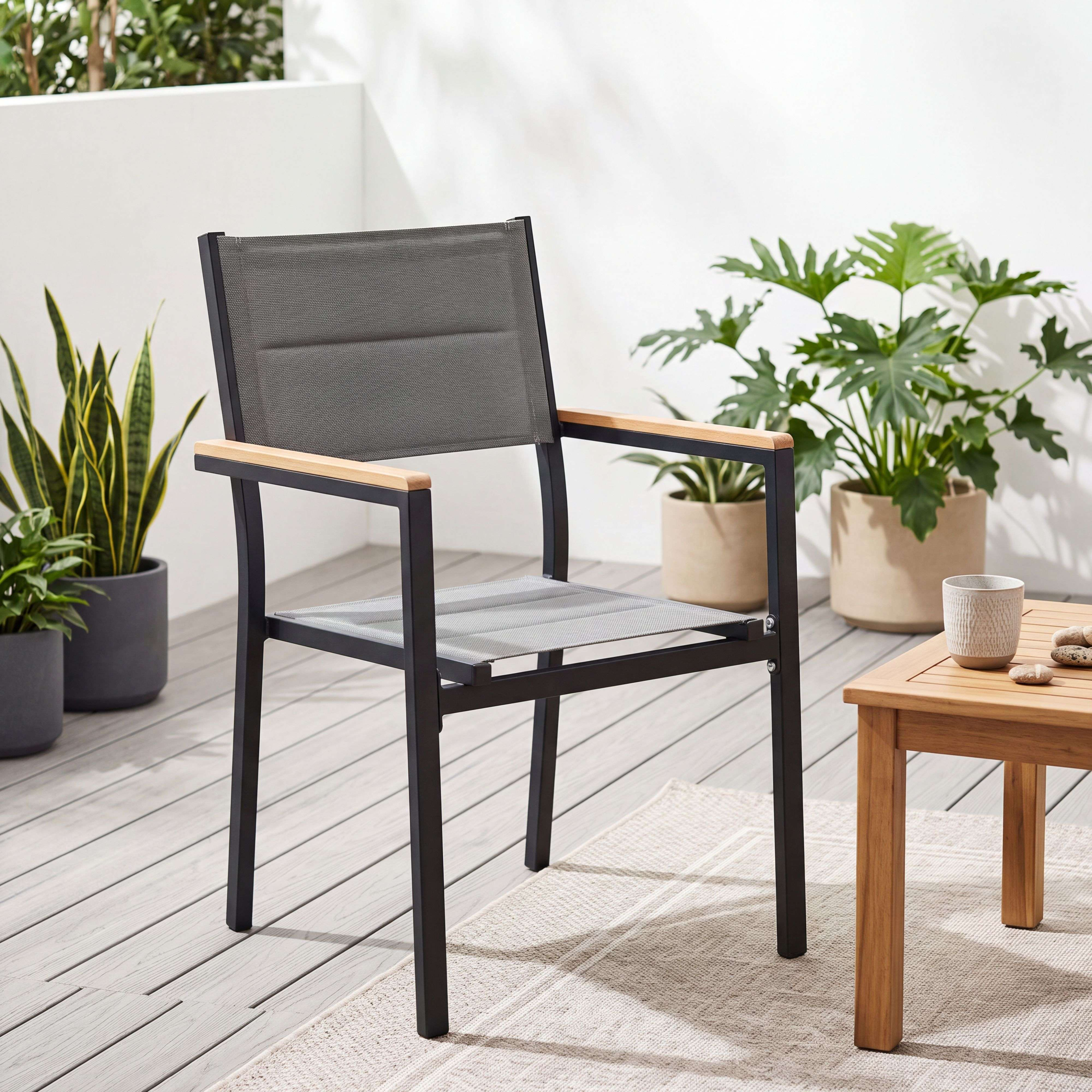 Una silla de exterior gris con brazos de madera descansa sobre una alfombra junto a una mesa de madera con una taza.