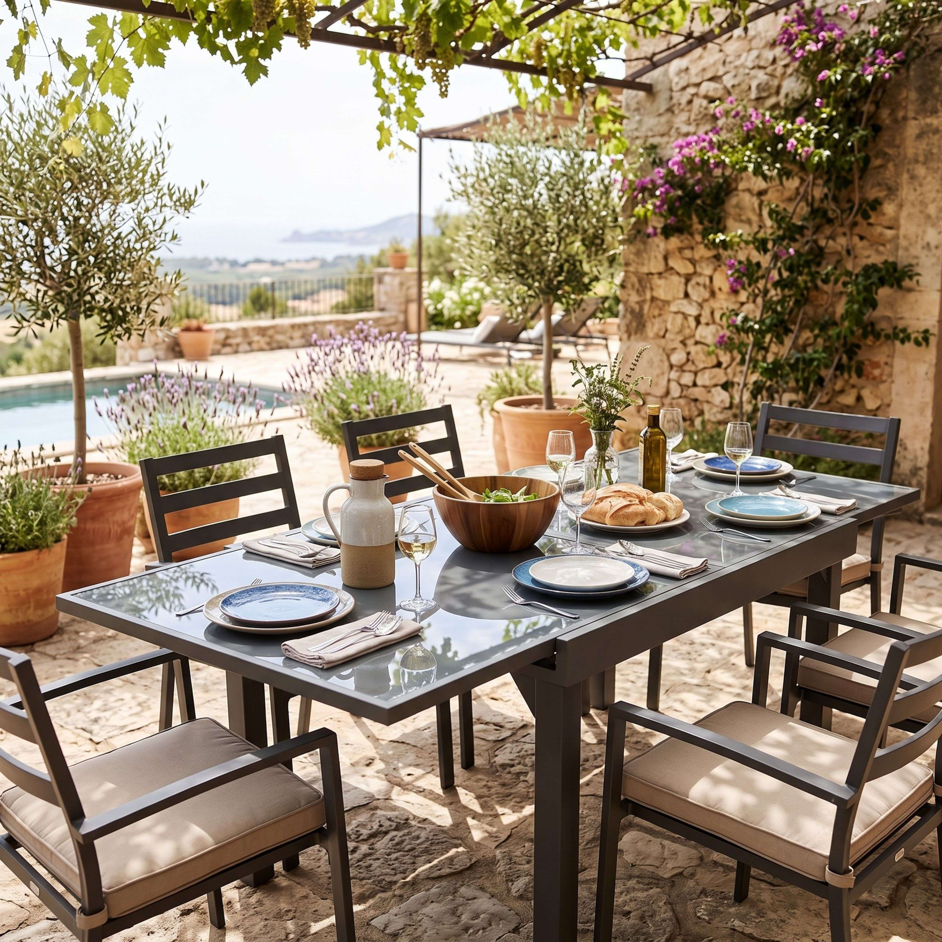 Una mesa de comedor exterior puesta con olivos, lavanda y una piscina al fondo.