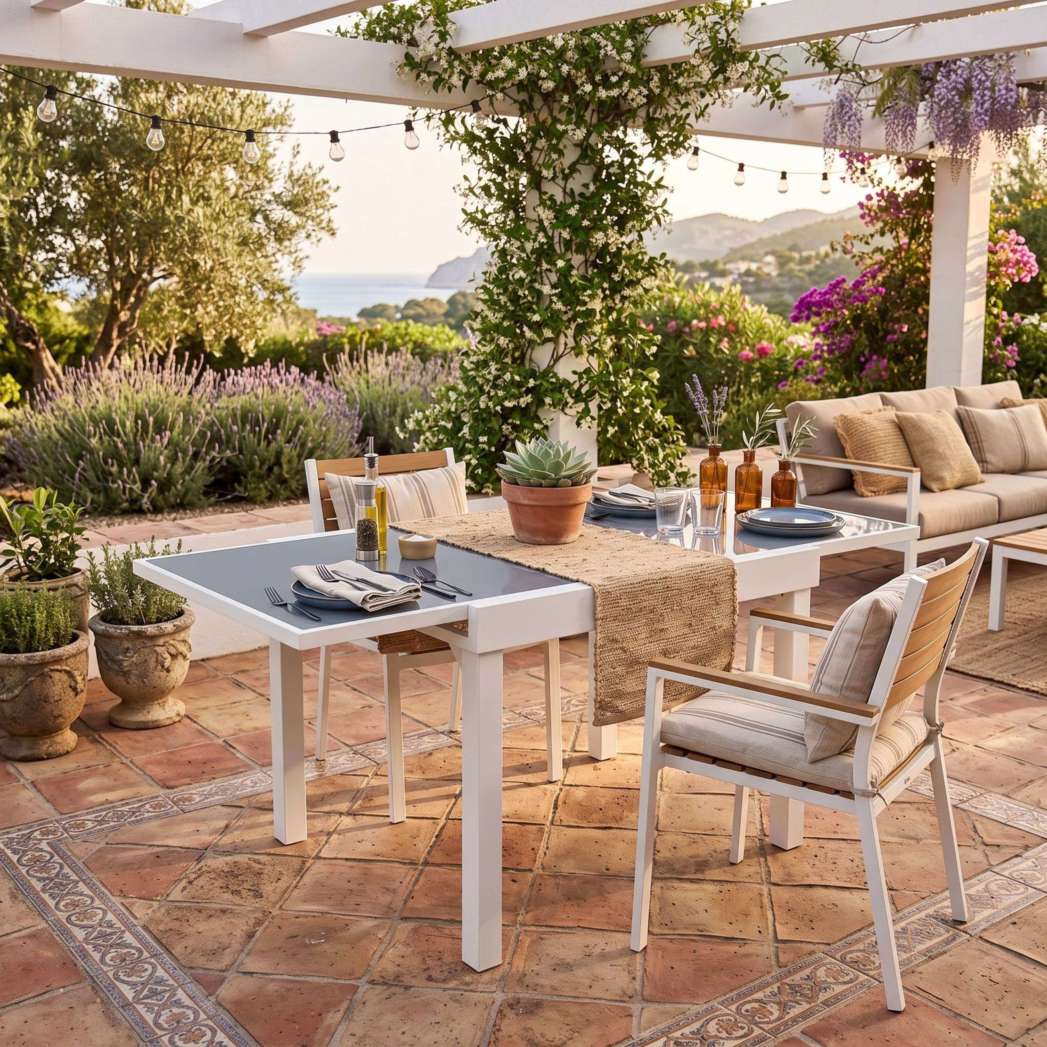 Un patio cubierto con mesa blanca, sillas, sofá y plantas florecientes.