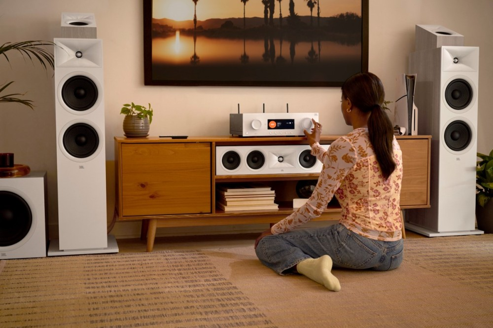 Kobieta siedzi na podłodze, regulując biały odbiornik audio obok dużych głośników.