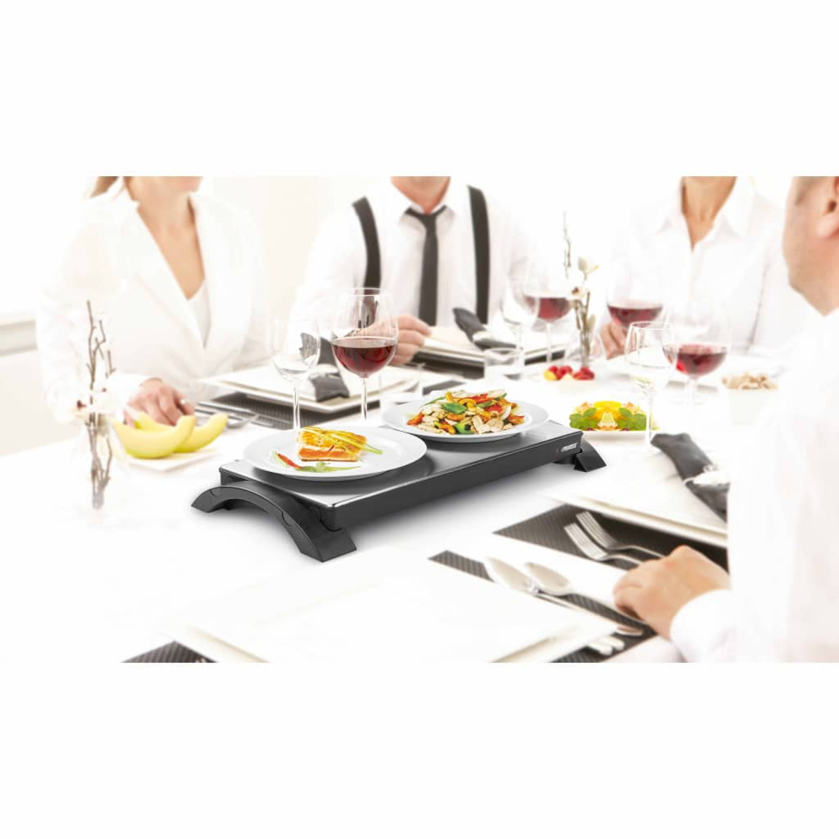 Menschen sitzen an einem Tisch mit Essen, darunter ein Serviergerät mit zwei Tellern.