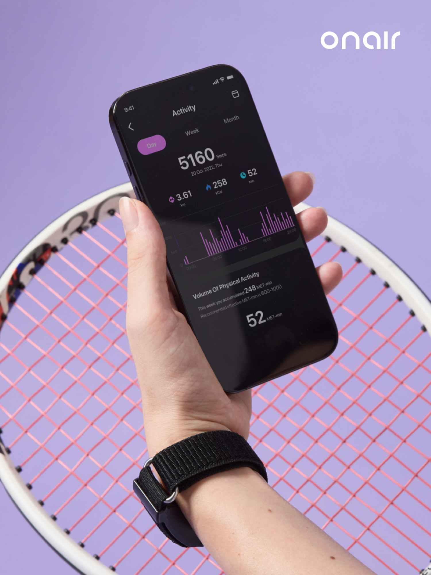 El, aktivite takip uygulamalı akıllı telefonu tutuyor, mor arka planda tenis raketi yanında.