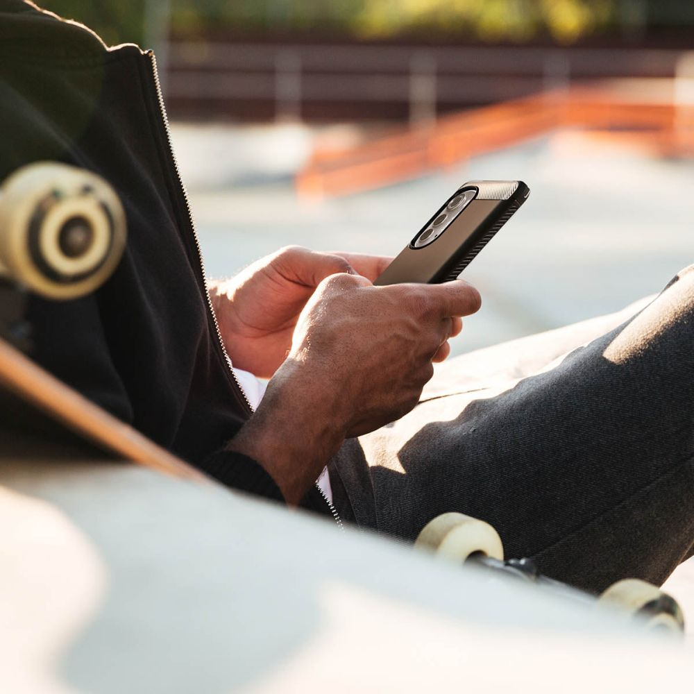 Una persona di colore seduta con un telefono in mano, accanto a uno skateboard.