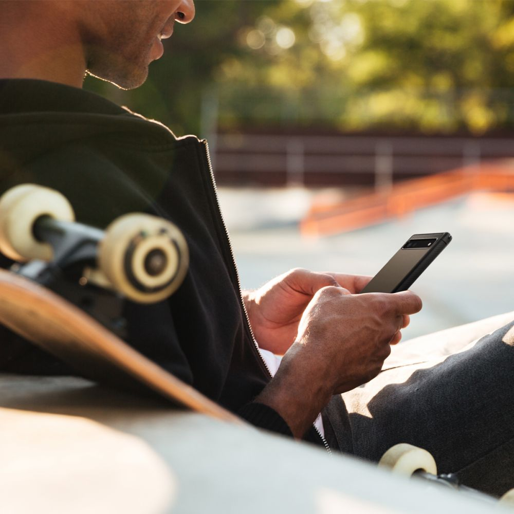 Uomo con skateboard usa smartphone all'aperto.