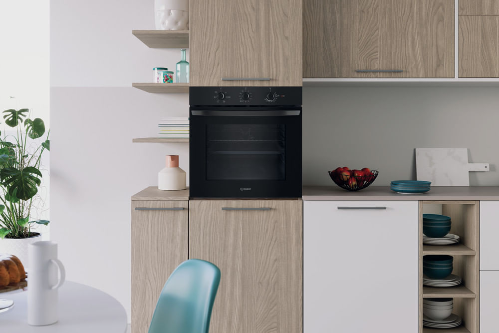 Cucina moderna con forno nero, mobili in legno, cesto di frutta e sedia verde acqua.