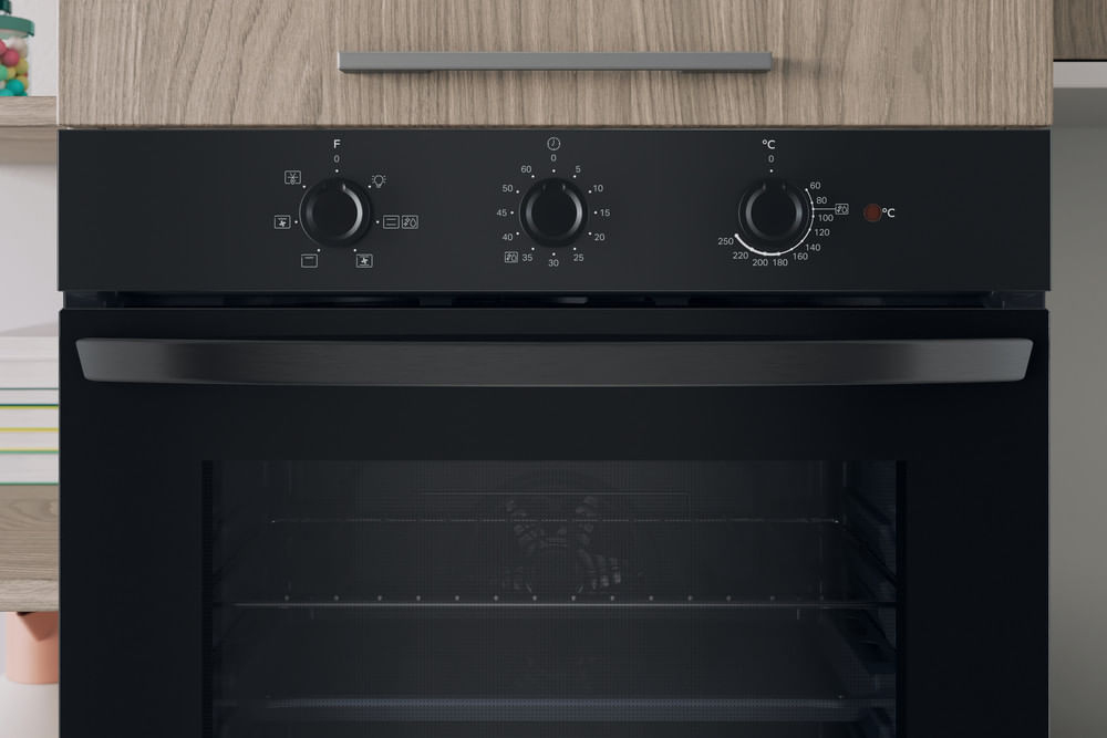 Primo piano di un pannello di controllo del forno nero con tre manopole e simboli.