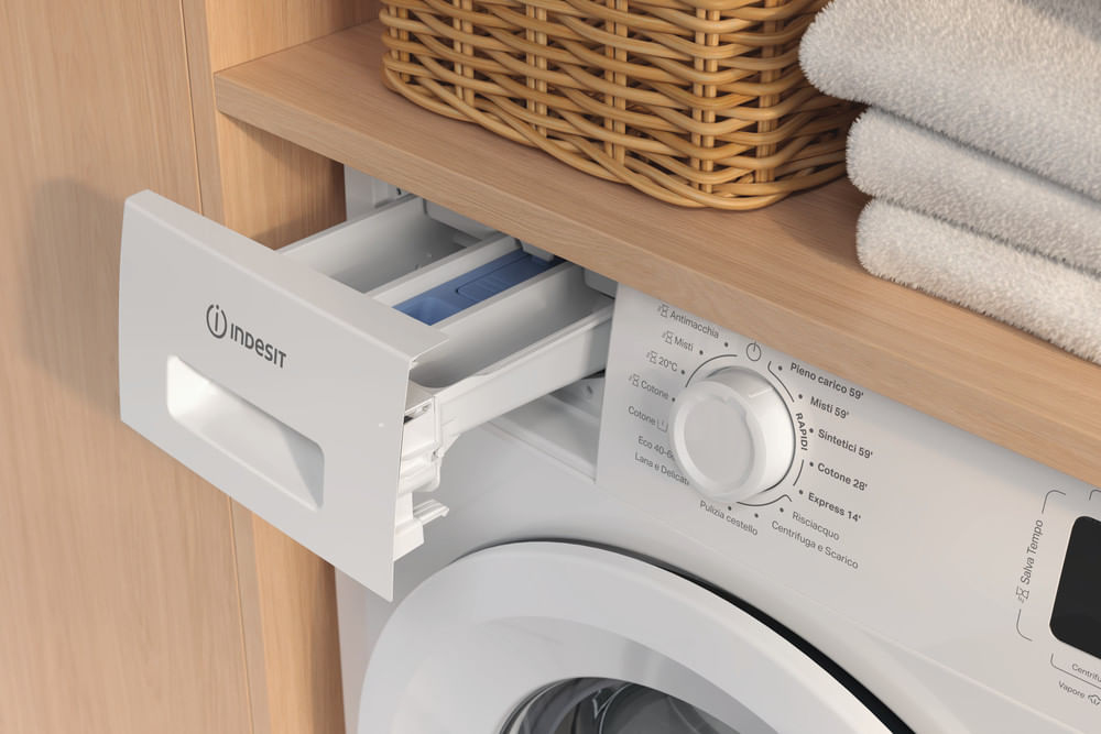 Il cassetto del detersivo di una lavatrice Indesit è estratto. Sopra ci sono asciugamani e un cesto.