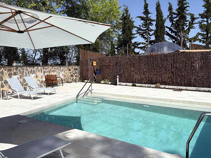 Un área de piscina al aire libre con tumbonas, sombrilla y muro de piedra.