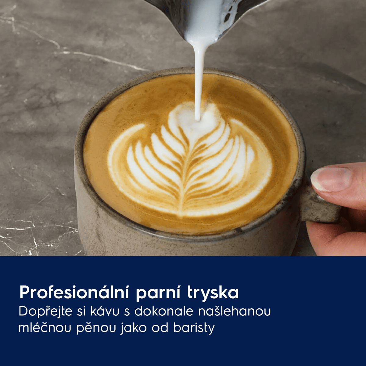 Latte art versato in una tazza con motivo a foglia. Una mano tiene la tazza.