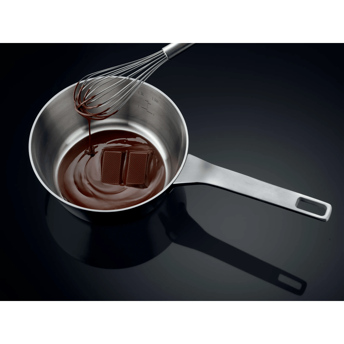 Chocolate derretida gotea de un batidor a una olla con dos trozos de chocolate.