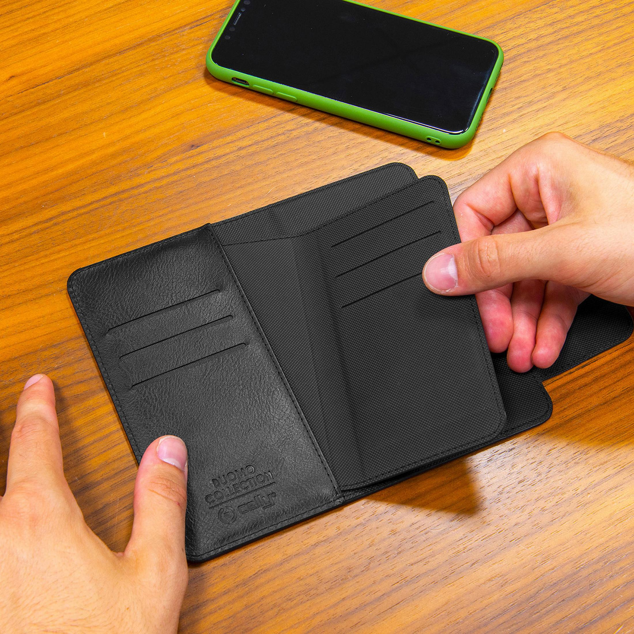 Mani che tengono un portafoglio nero su un tavolo di legno accanto a uno smartphone verde.