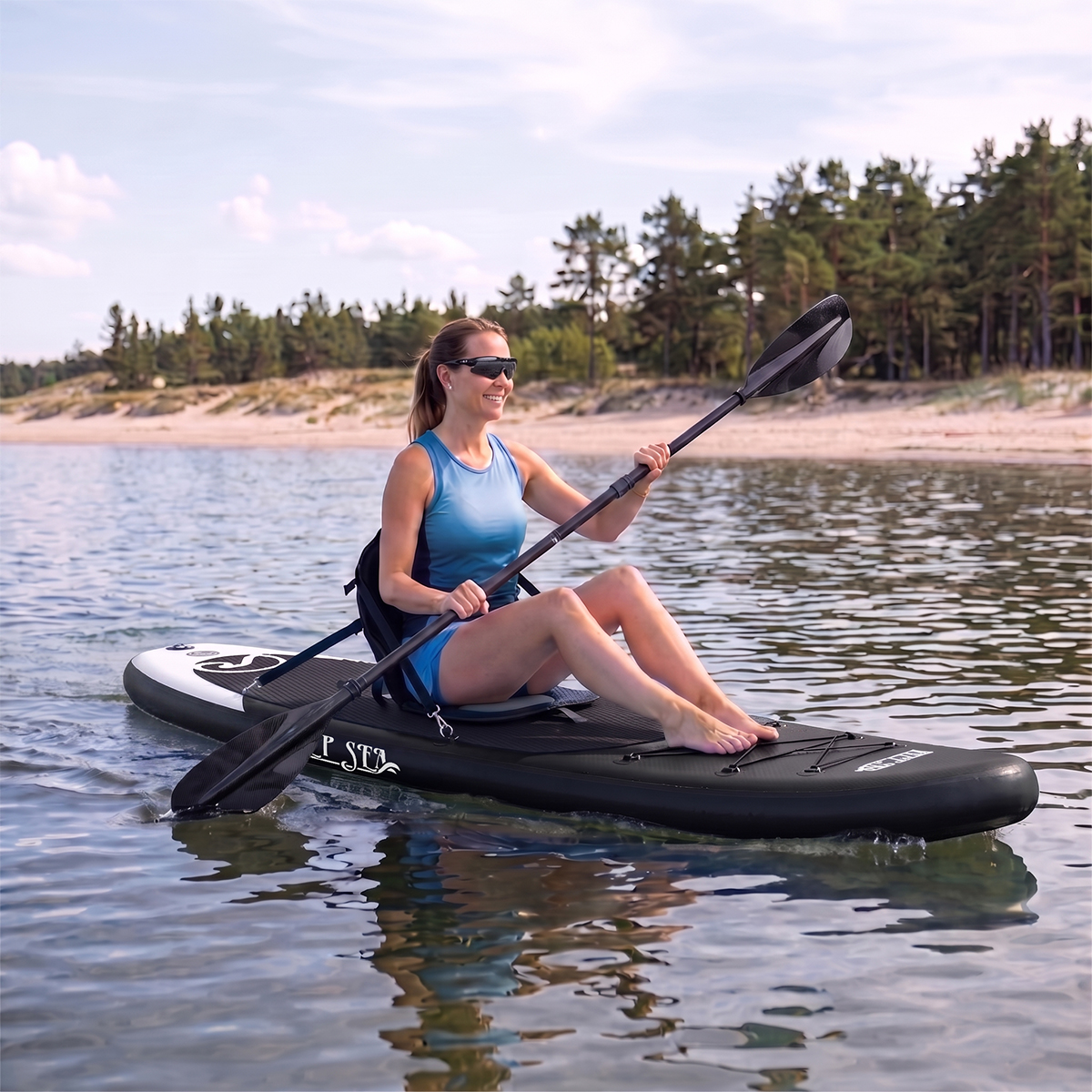 Kobieta pływa na desce z wiosłem po spokojnej wodzie blisko piaszczystej plaży z drzewami.