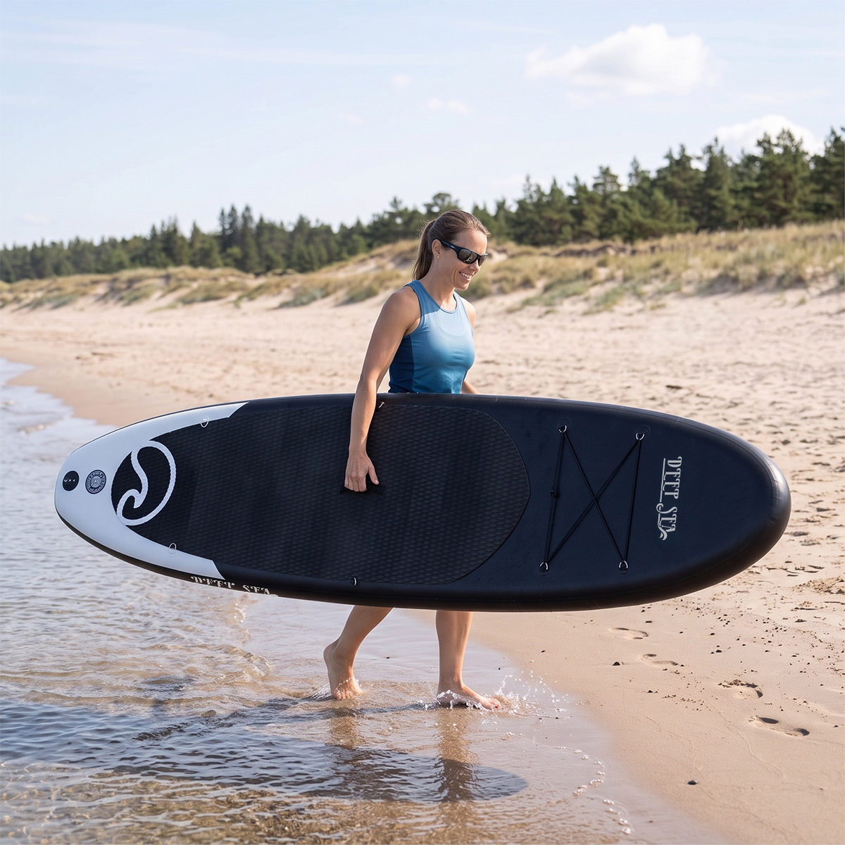 Kobieta niesie czarną deskę SUP na plaży.