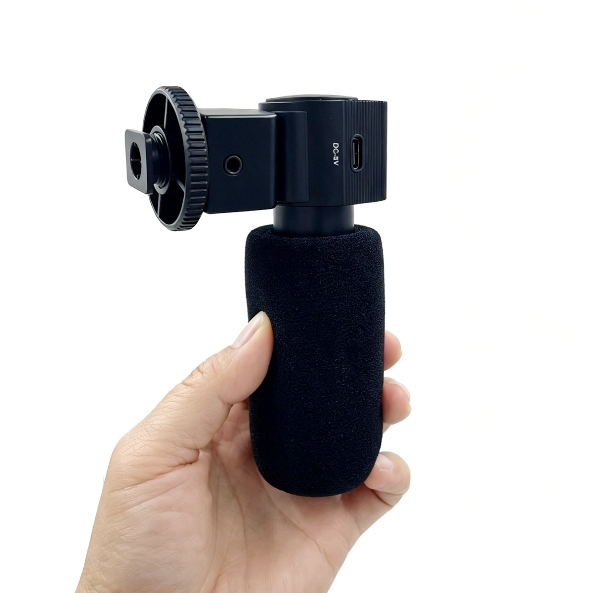 Una mano tiene un microfono nero con impugnatura in schiuma e supporto per fotocamera.