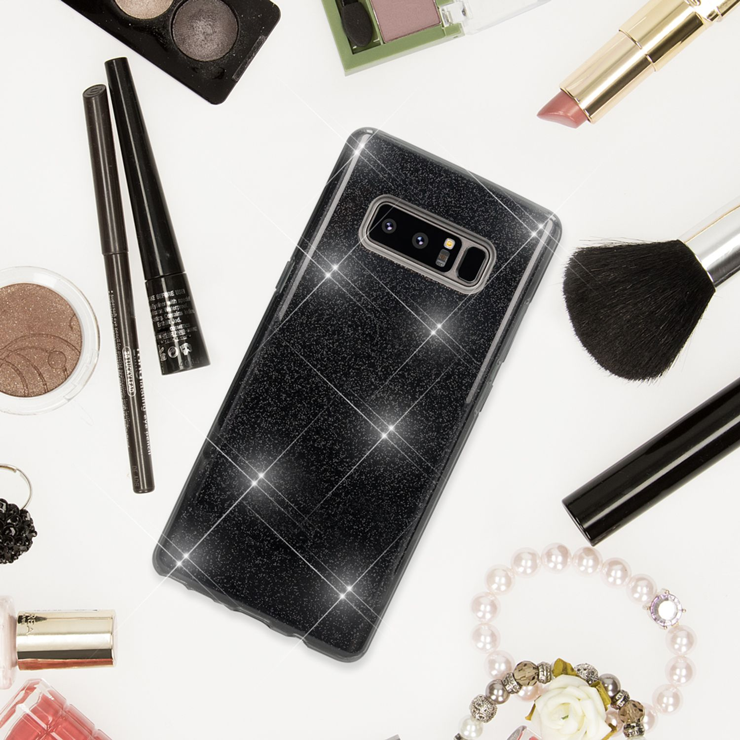 Ein glitzerndes schwarzes Handy auf einem weißen Hintergrund, umgeben von Kosmetika.